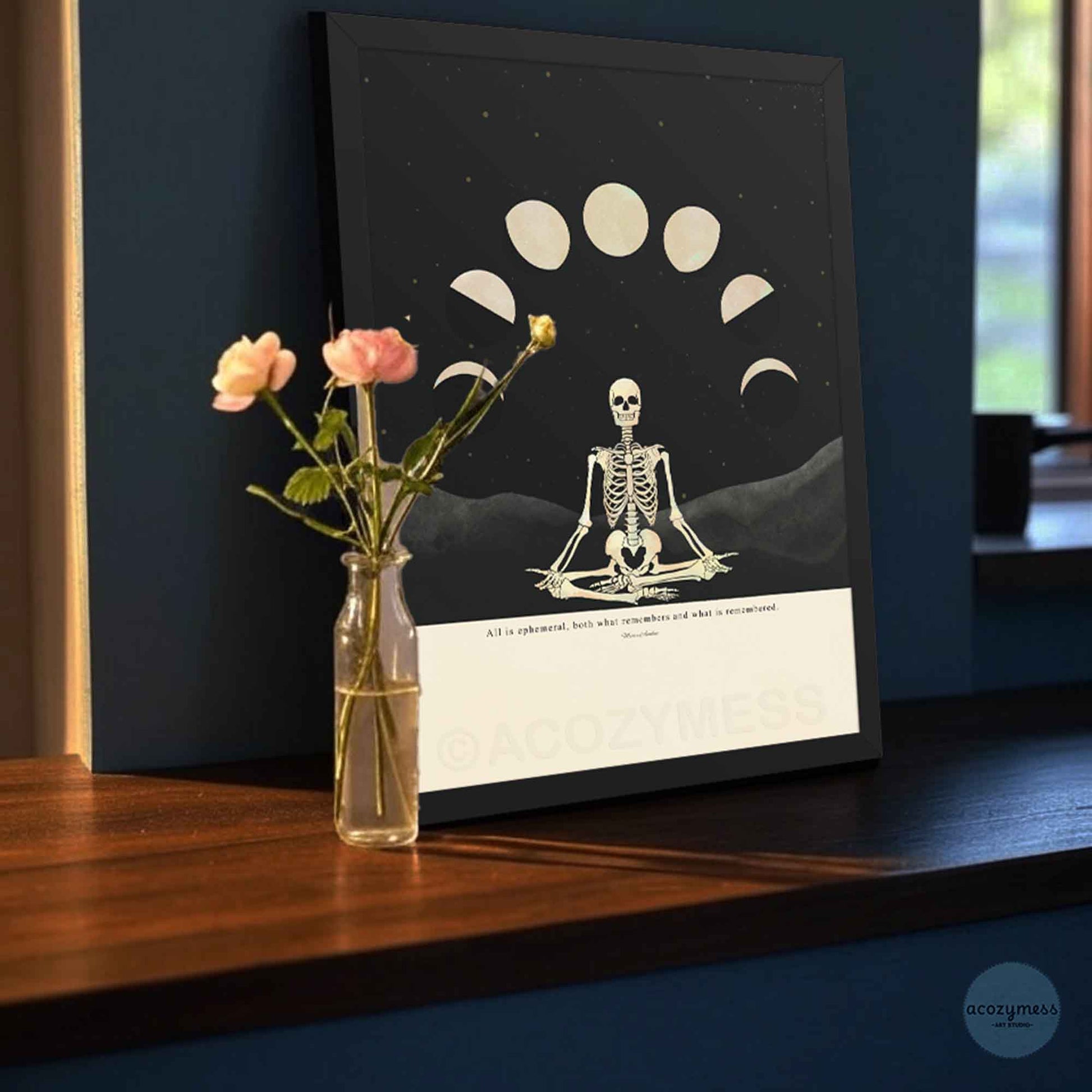 Framed Marcus Aurelius stoic quote poster with skeleton and moon phase illustration, printed on beige background and displayed in sleek black wooden frame.