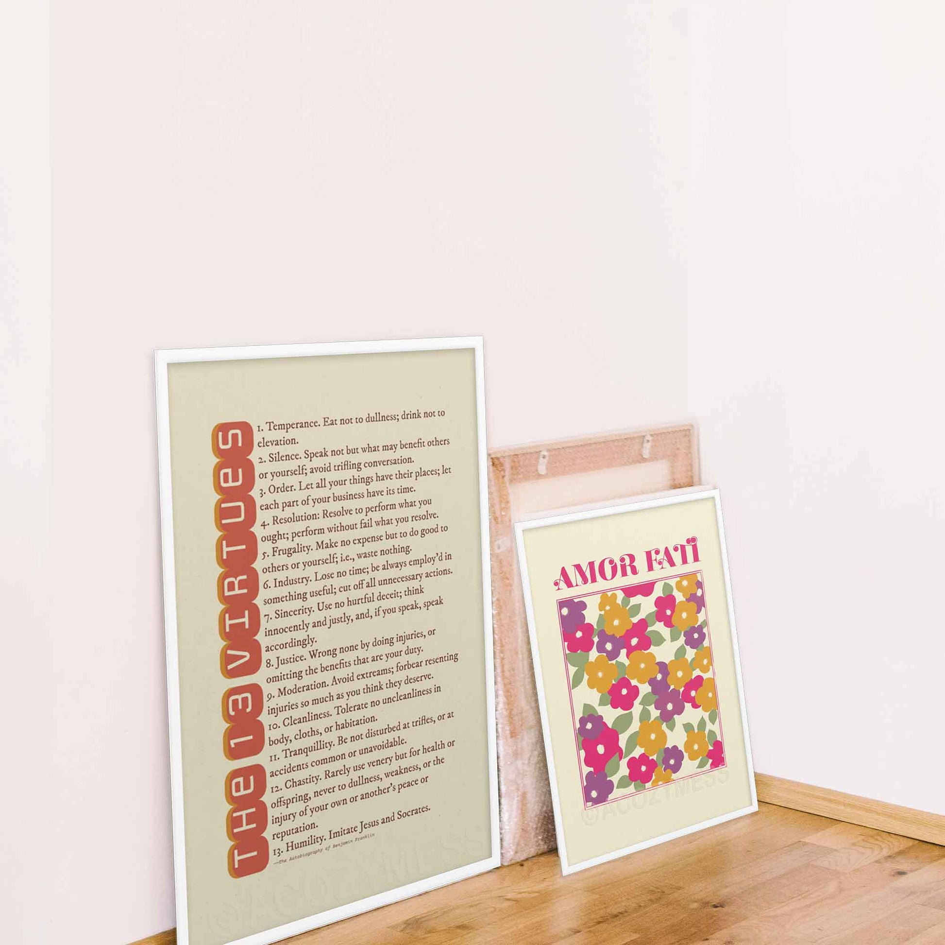 13 Virtues by Benjamin Franklin poster in red on beige, displayed in a oakwood frame. And Amor fati colorful abstract flower design in white frame.