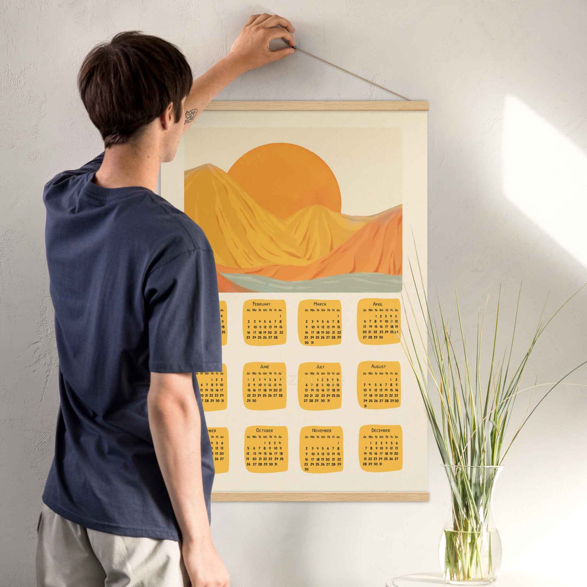 2025 illustrated calendar featuring a serene morning scene in yellow and orange tones, displayed with an oakwood hanger, perfect for adding warmth and charm.