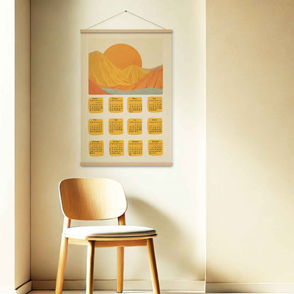 2025 illustrated calendar featuring a morning sun behind mountains in yellow and orange tones, displayed with an oakwood hanger on a entryway wall, perfect for adding warmth and interest.