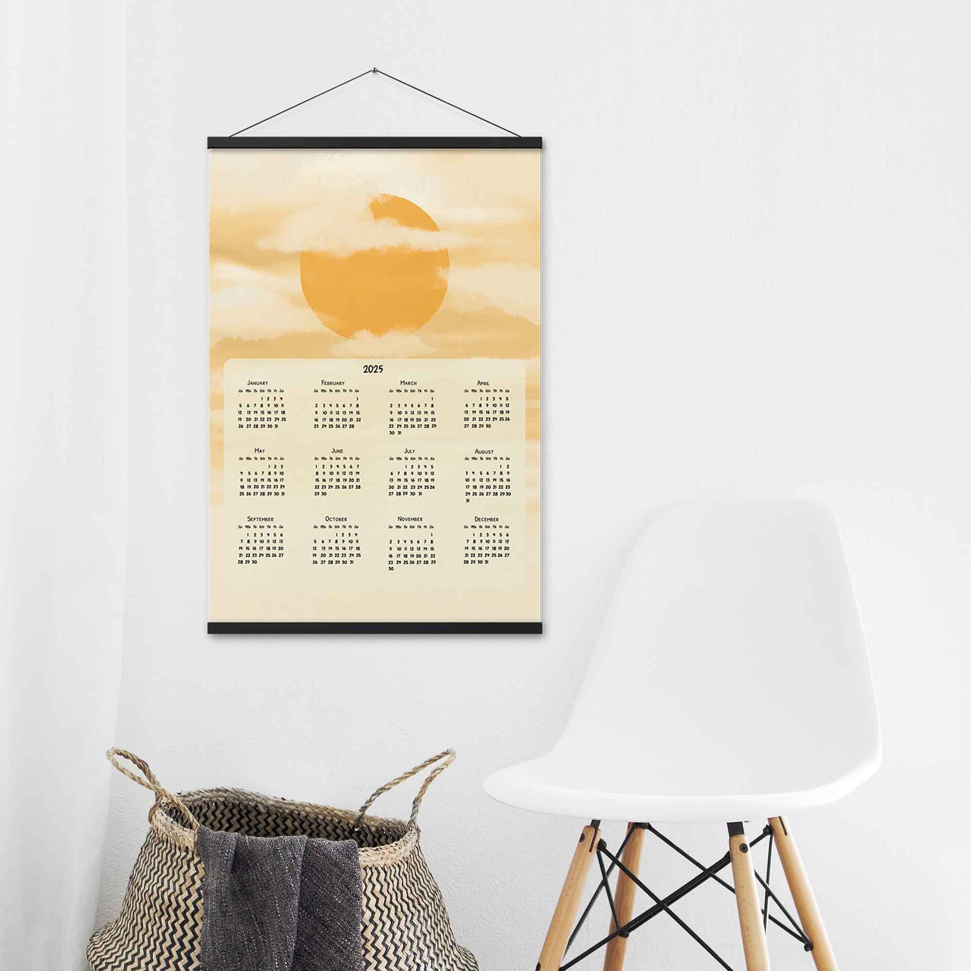 2025 yearly wall calendar featuring a sun and clouds illustration on a muted yellow background, adding warmth to the design, displayed in a black hanger frame on an laundry room wall.