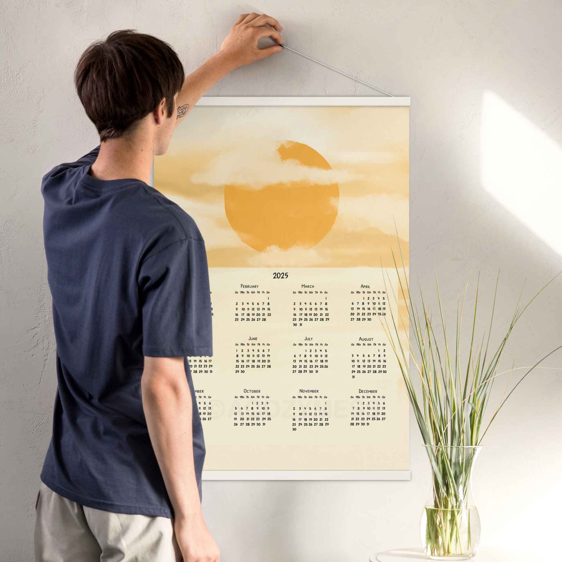 2025 yearly wall calendar featuring a sun and clouds illustration on a muted yellow background, adding warmth to the design, displayed in a white hanger frame.