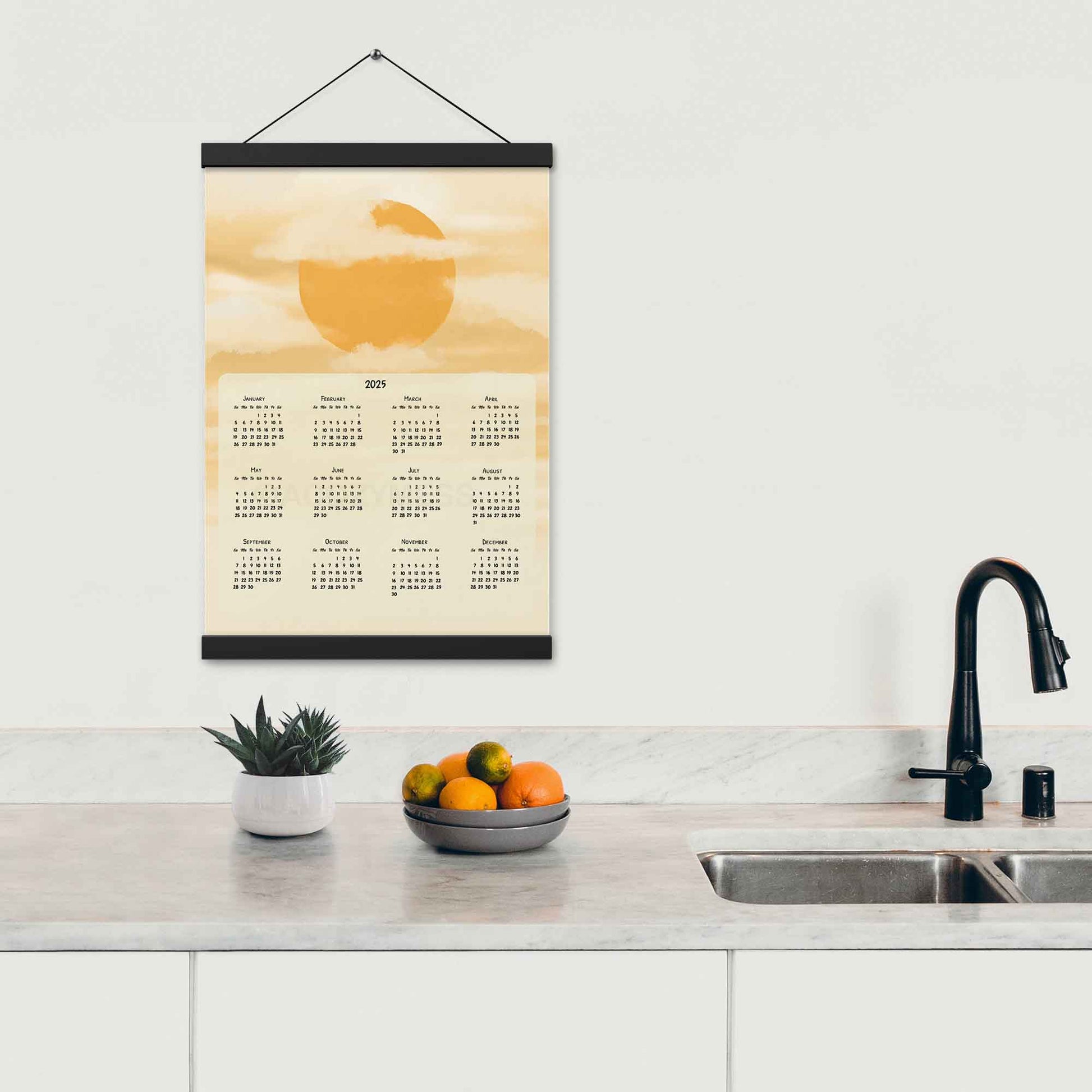 2025 yearly wall calendar featuring a sun and clouds illustration on a muted yellow background, adding warmth to the design, displayed in a black hanger frame on a kitchen wall.