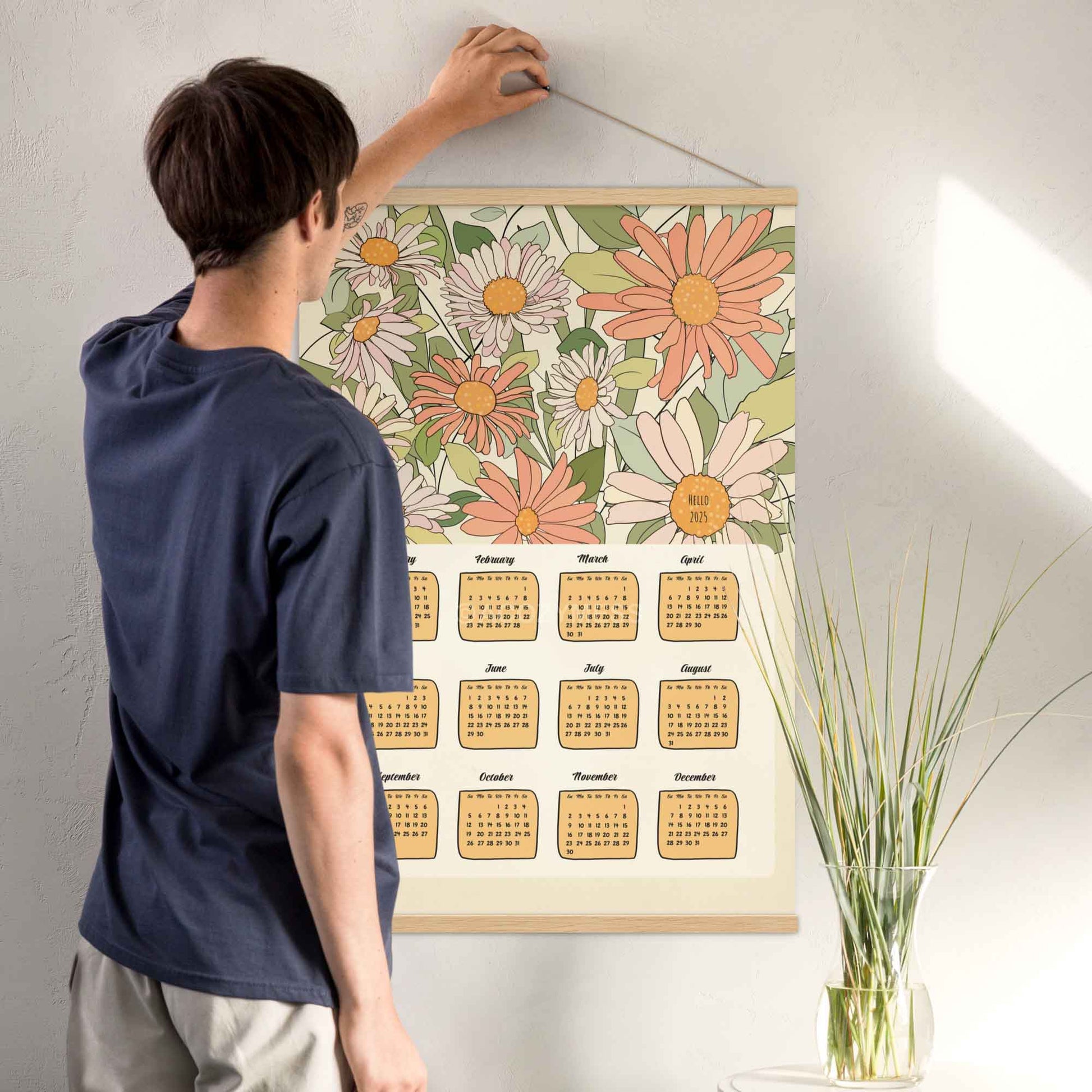 Illustrated 2025 calendar with flower design in beige, green, pink, and orange colors, featuring an oakwood hanger. 