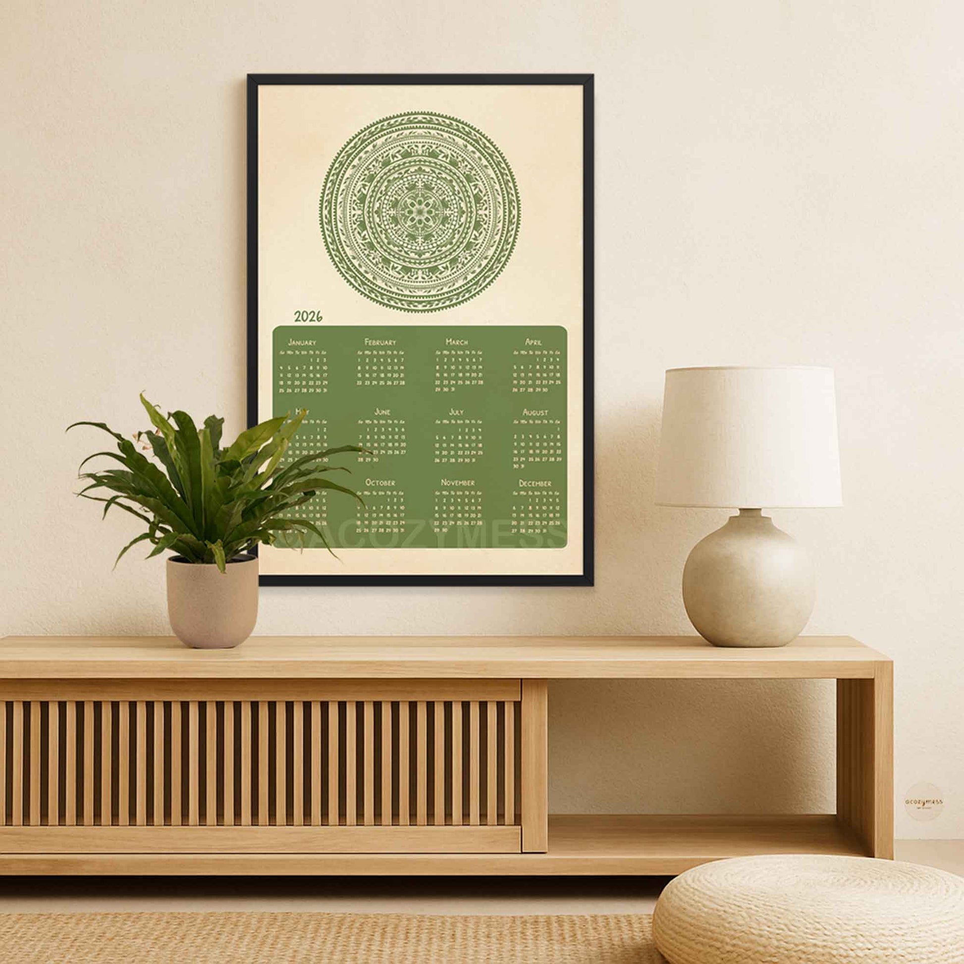 Framed green calendar 2026 on a wall above a wooden console table with a plant and lamp.