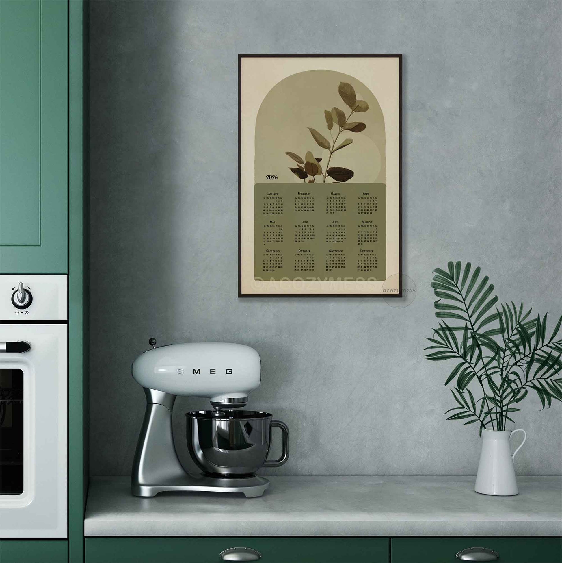 One page calendar 2026 with nature inspired art in green and beige in black frame displayed on a kitchen wall