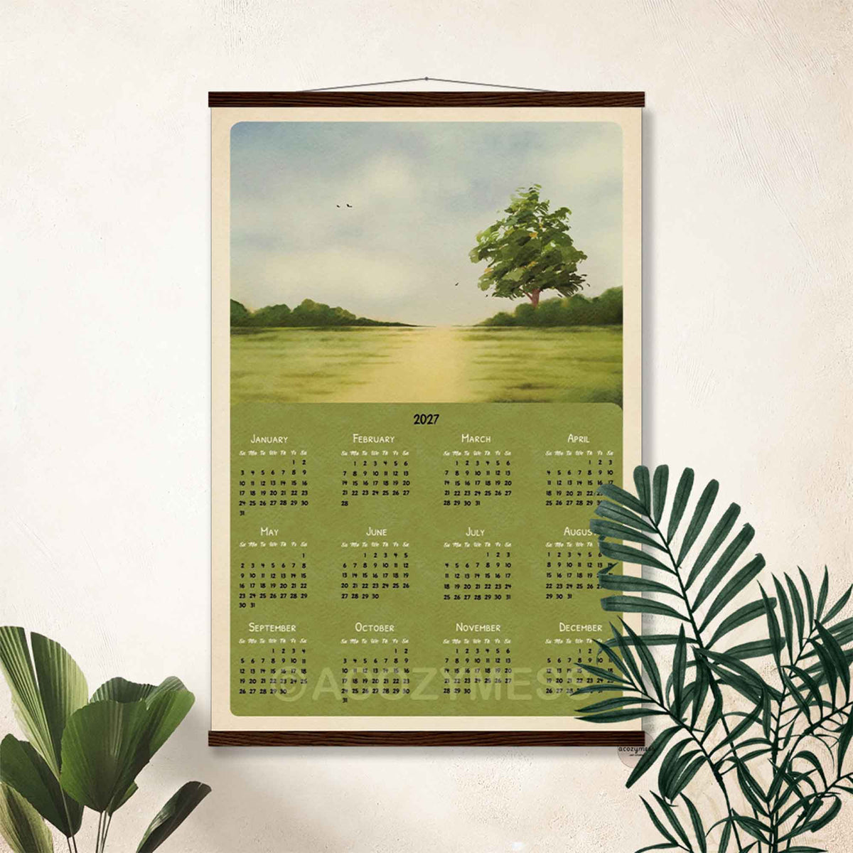 2027 green meadow calendar poster in a dark wooden hanger frame on a cream wall with palm leaves
