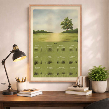 Oak framed 2027 green meadow calendar above a desk with a black lamp, books and a potted plant