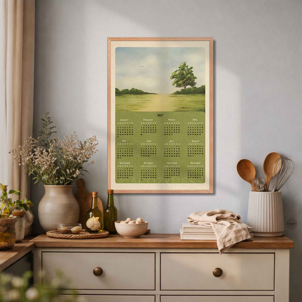 Light wood framed 2027 landscape calendar above a cream kitchen sideboard with vases and wooden spoons