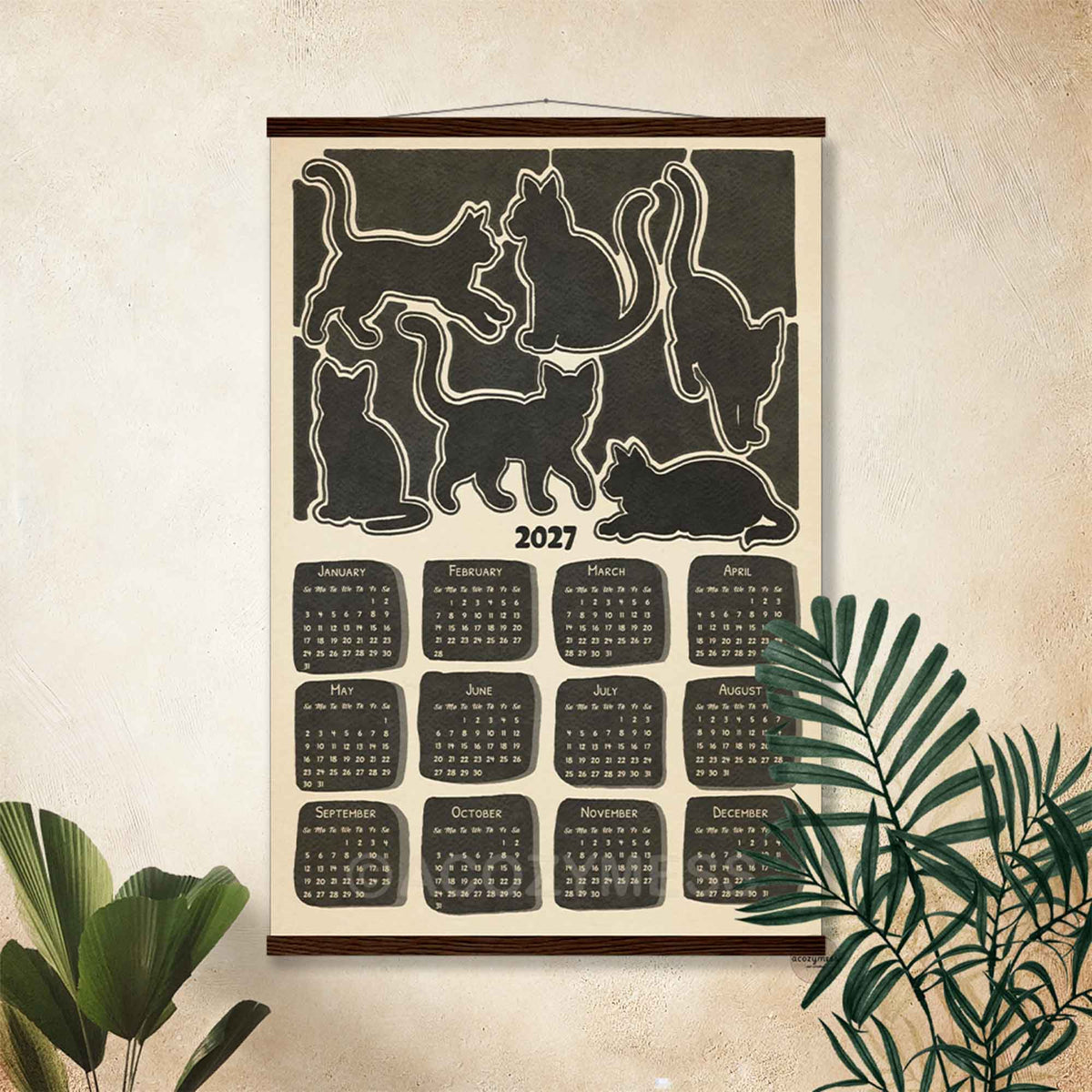 2027 black cat silhouette calendar poster in a dark wooden hanger frame on a beige wall with palm leaves