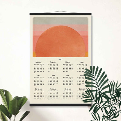 2027 sunset calendar poster in a black hanger frame on a white wall with palm leaves