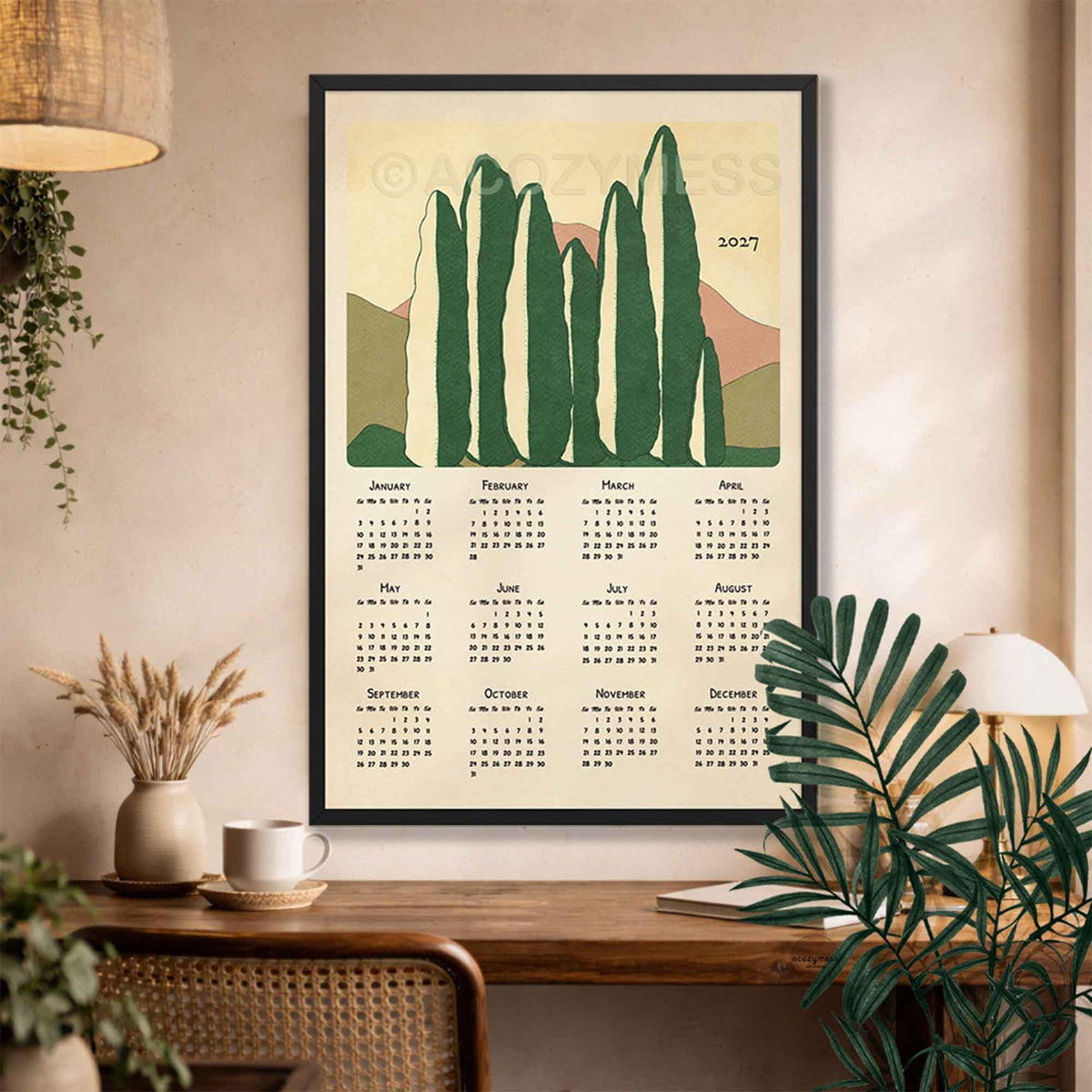 Black framed 2027 cypress trees calendar above a desk with a rattan chair, dried grasses and palm leaves