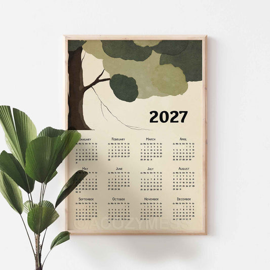 Oak framed 2027 green tree calendar poster on a white wall beside a fan palm plant