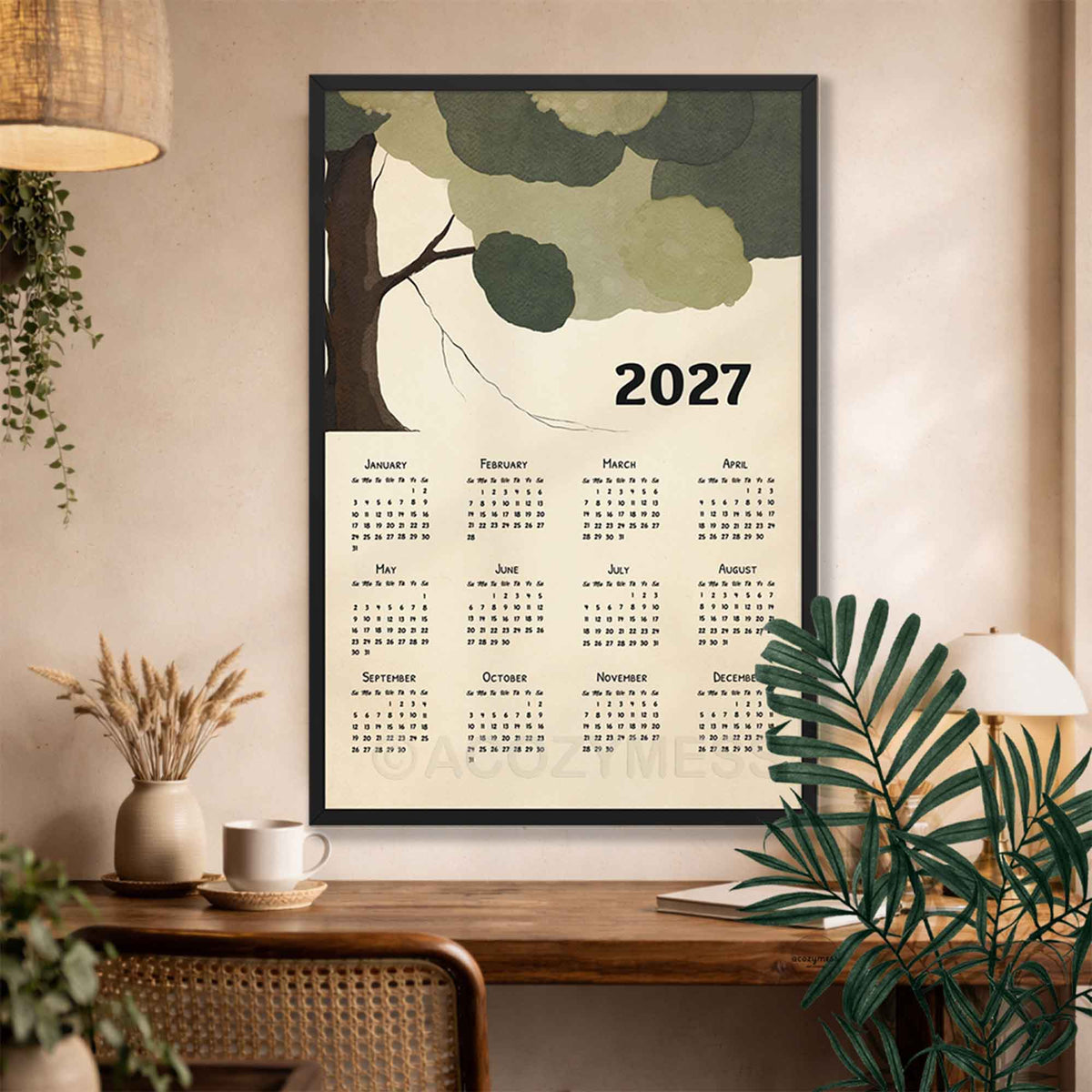 Black framed 2027 botanical tree calendar above a desk with a rattan chair, dried grasses and palm leaves