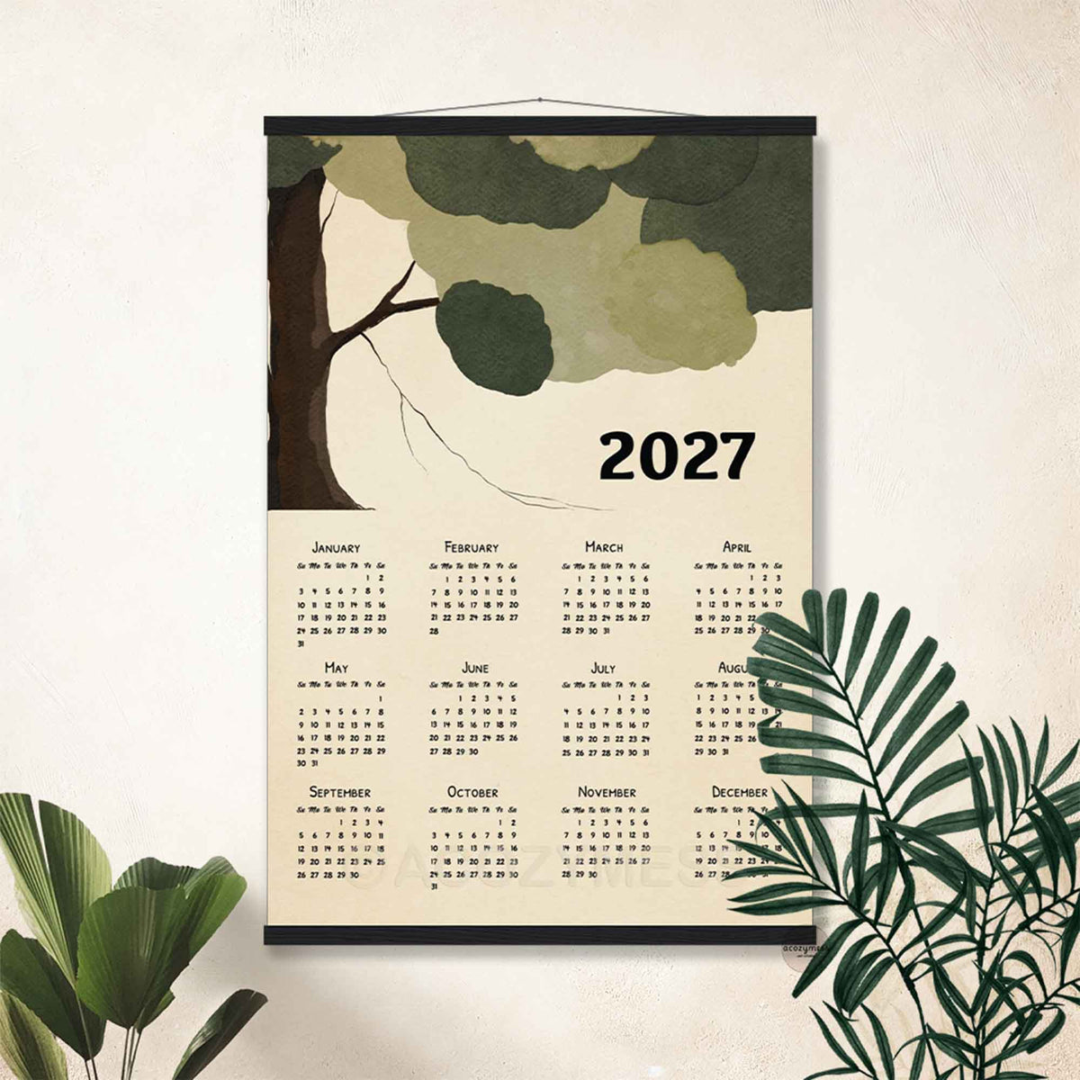 2027 green tree calendar in a black hanger frame on a white wall with tropical plants