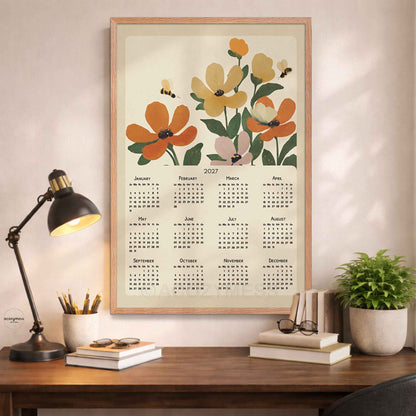 Oak framed 2027 flower calendar print above a wooden desk with a black lamp, books and a potted plant