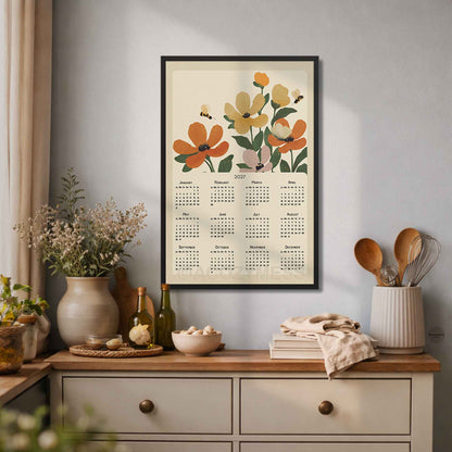 Black framed 2027 flowers and bees calendar poster above a cream dresser with vases and kitchen utensils