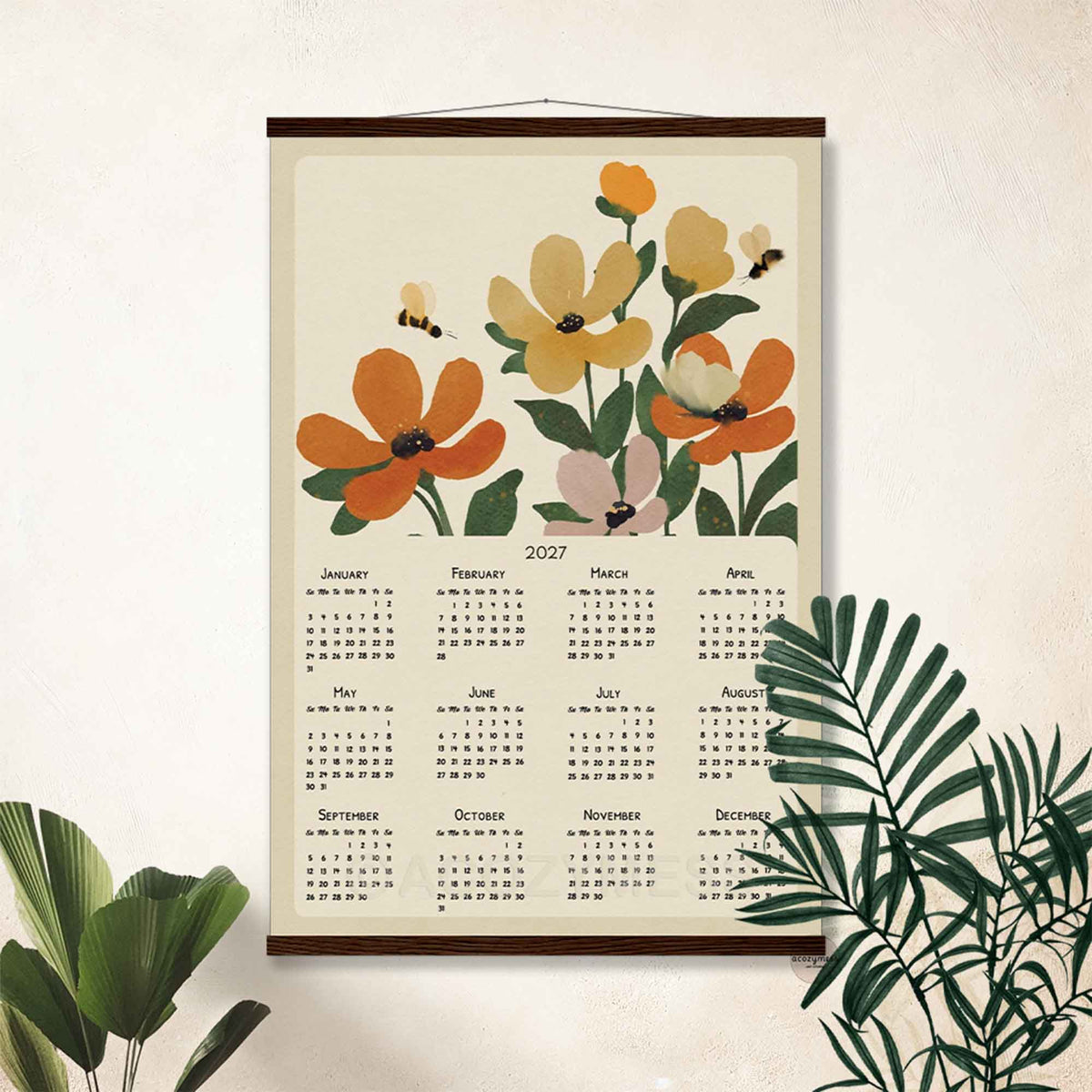 2027 floral calendar in a dark wood hanger frame on a white wall with tropical plants