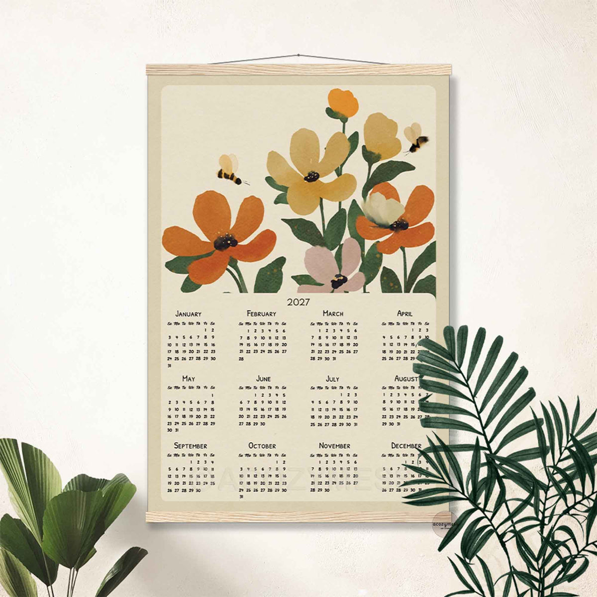 2027 orange flower calendar print in a light wood hanger frame on a white wall with palm leaves