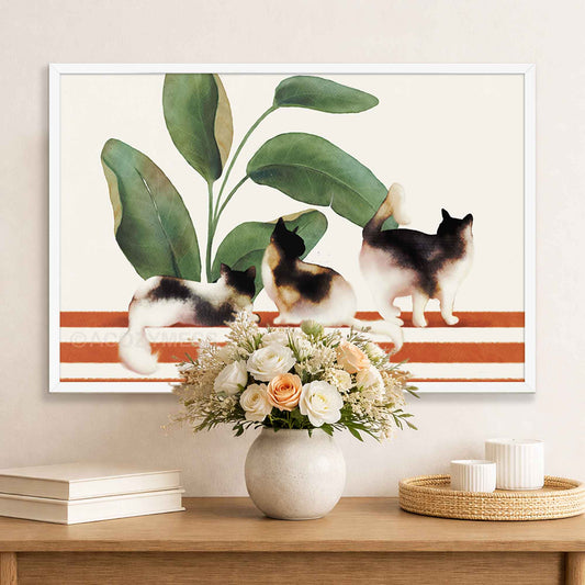 Framed artwork of three cats on a striped bench with plants, displayed above a table with a vase and flowers.