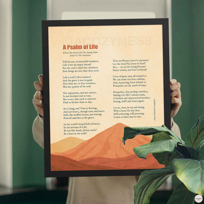 Hands holding a black framed A Psalm of Life poem print with burnt orange mountain art against a green wall
