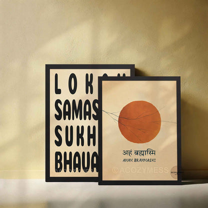 Two framed wall art prints leaning against a beige wall. The left print has bold black lokah samastah mantra  on a cream background, and the right print shows a large orange sun illustration with aham brahmasmi mantra below.