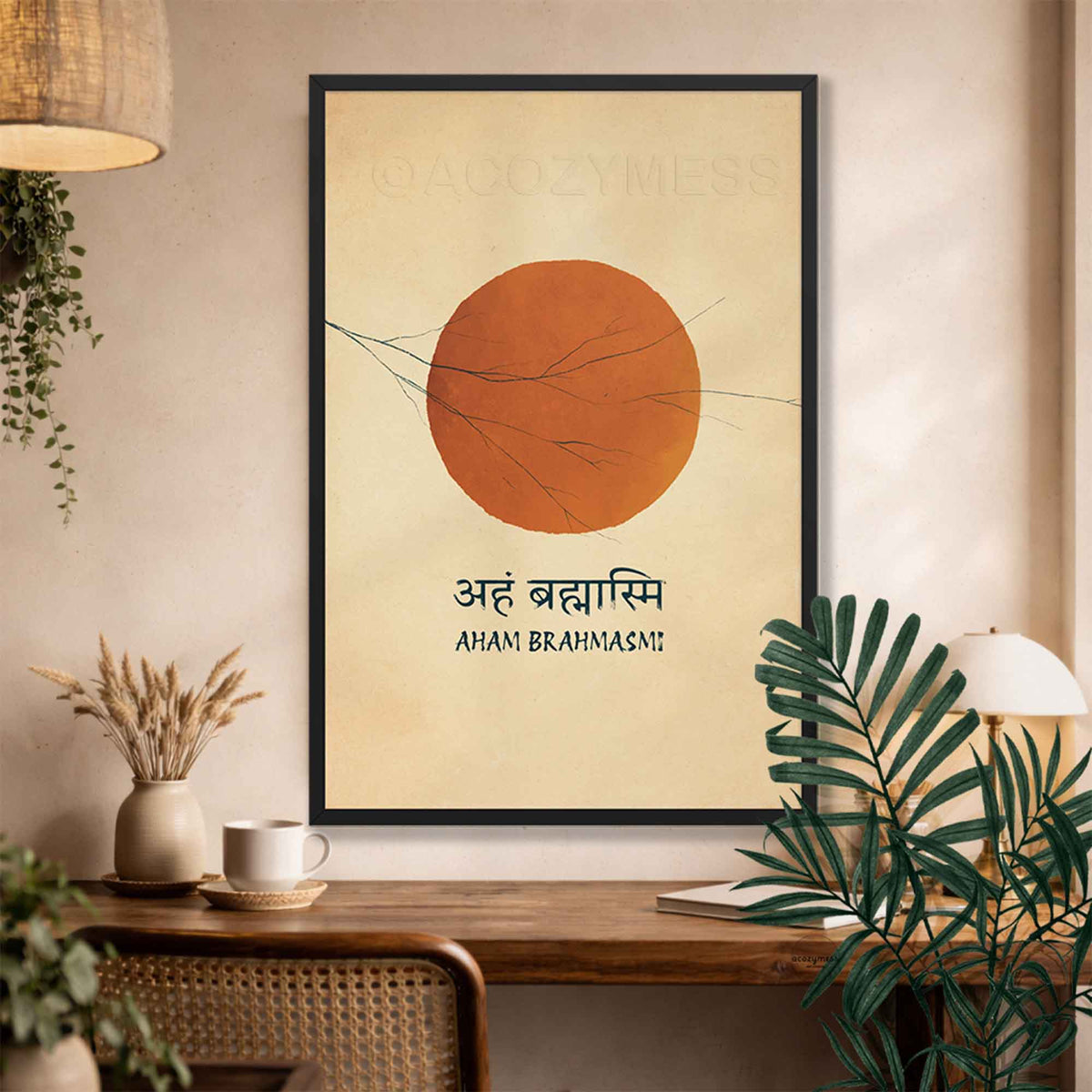 A framed minimalist art print featuring a large terracotta orange sun on a warm beige background with the text 'AHAM BRAHMAS!' and Devanagari script, displayed on a wooden console table in a styled room with plants and home decor.
