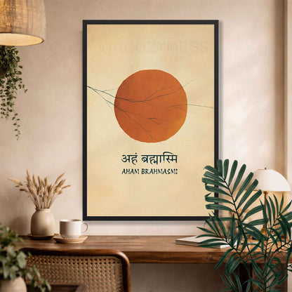 A framed minimalist art print featuring a large terracotta orange sun on a warm beige background with the text 'AHAM BRAHMAS!' and Devanagari script, displayed on a wooden console table in a styled room with plants and home decor.
