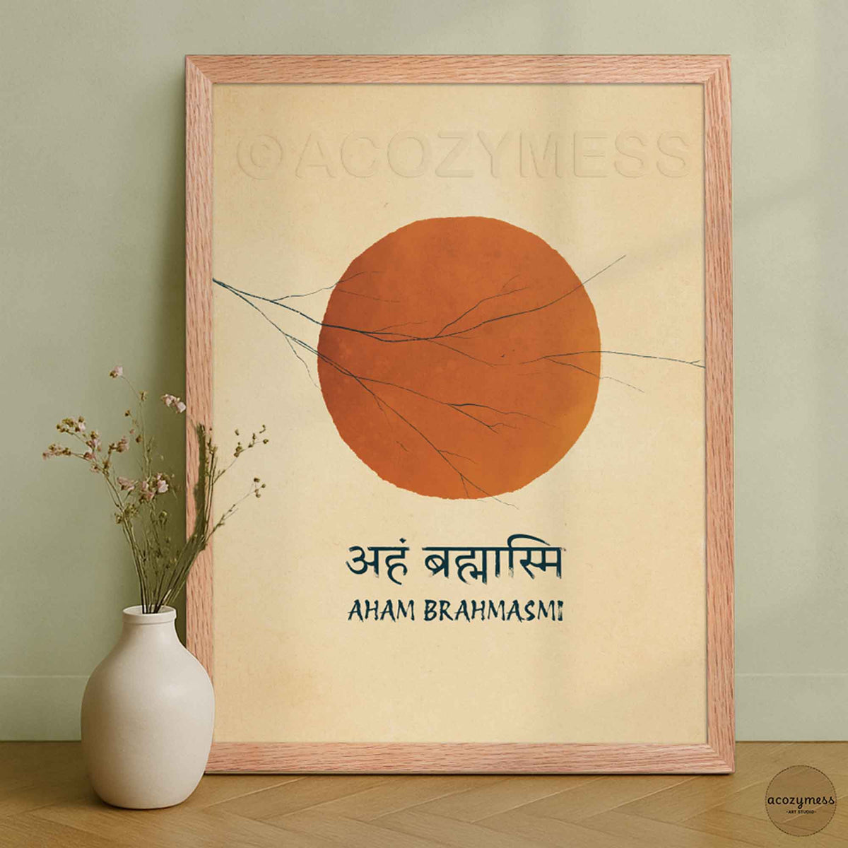 A framed art print featuring a large orange sun with thin black branch-like lines and the text 'Aham Brahmasi' in Devanagari and English, leaning against a light green wall next to a small white vase.