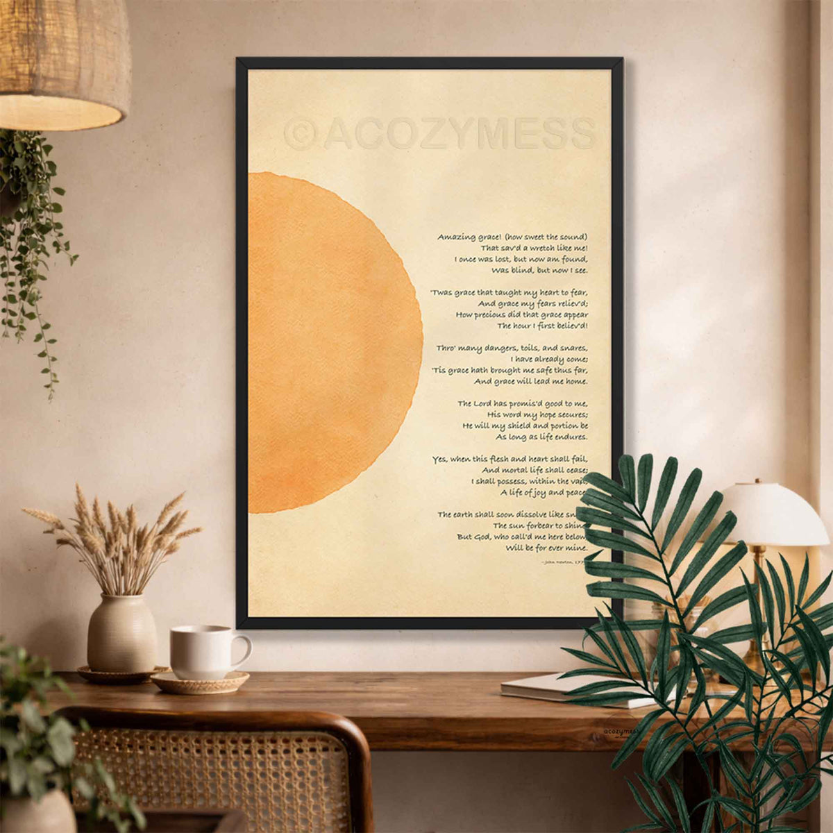A framed wall art print featuring a christian hymn  on a warm cream background with a large muted gold abstract sun on the left, hanging on a beige wall above a wooden console table with plants and decor.
