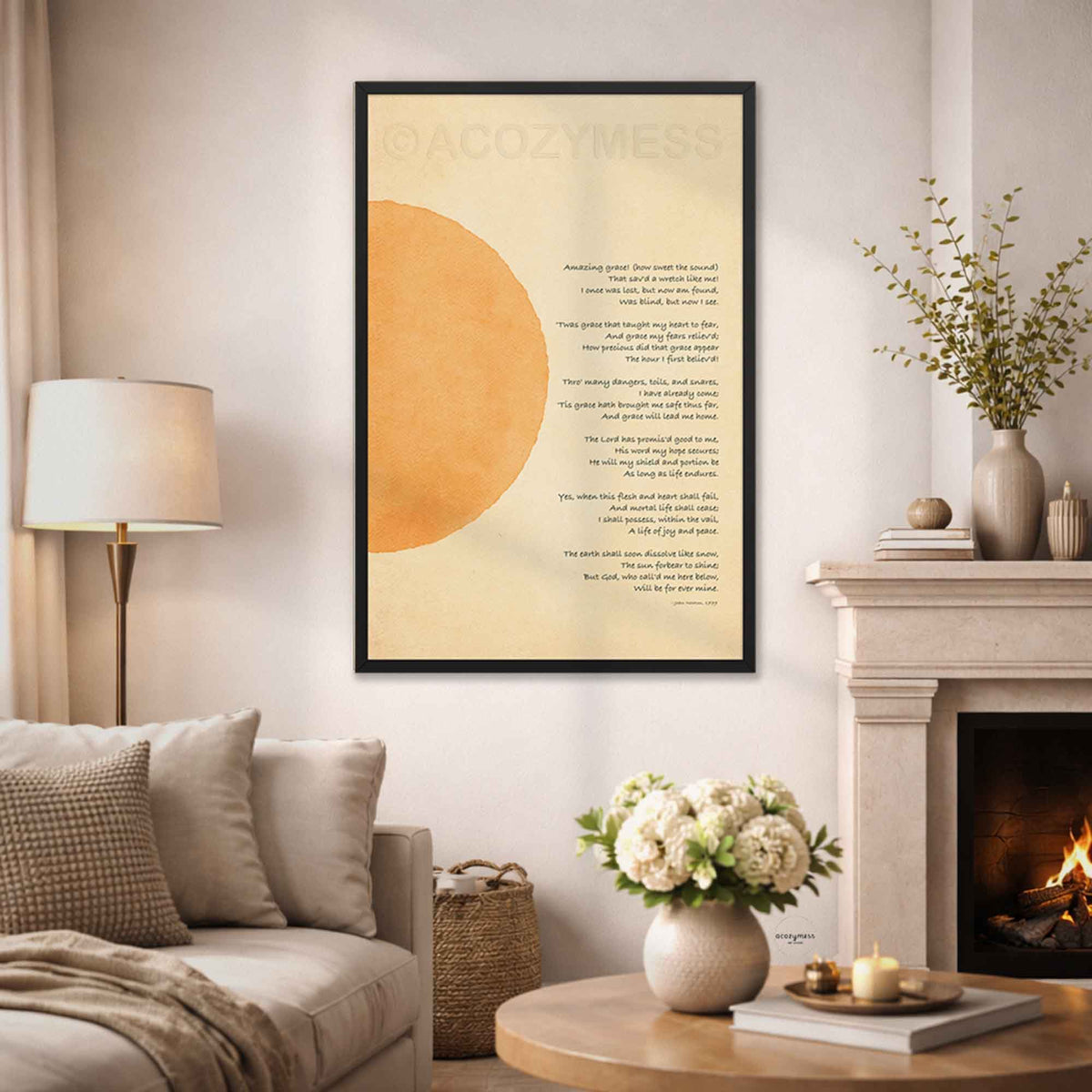 A framed wall art print hangs above a sofa in a styled living room. The print features a large warm sun on a cream background with christian hymn - amazing grace.