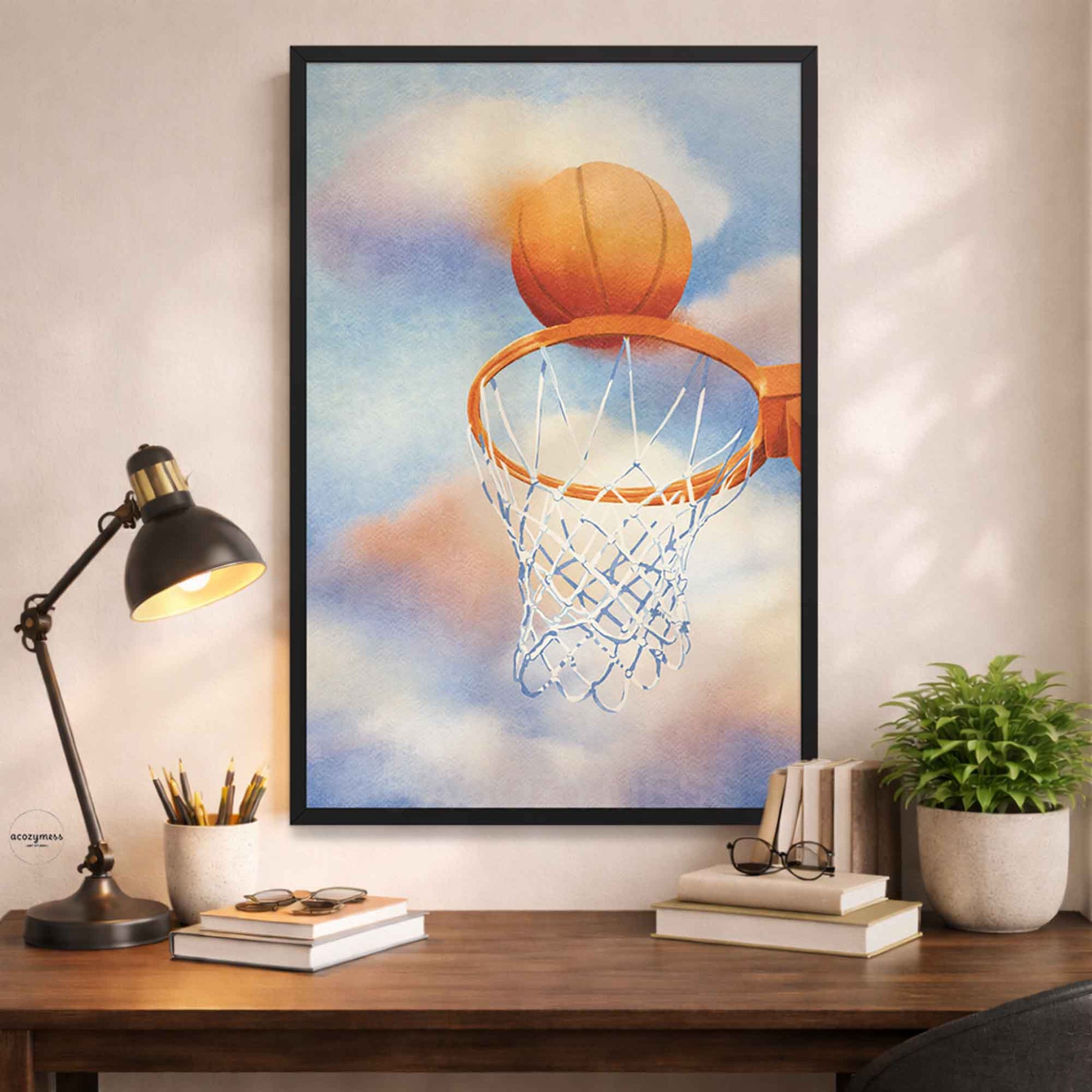 Framed artwork of a basketball going through a hoop on a wall above a desk with a lamp and books.