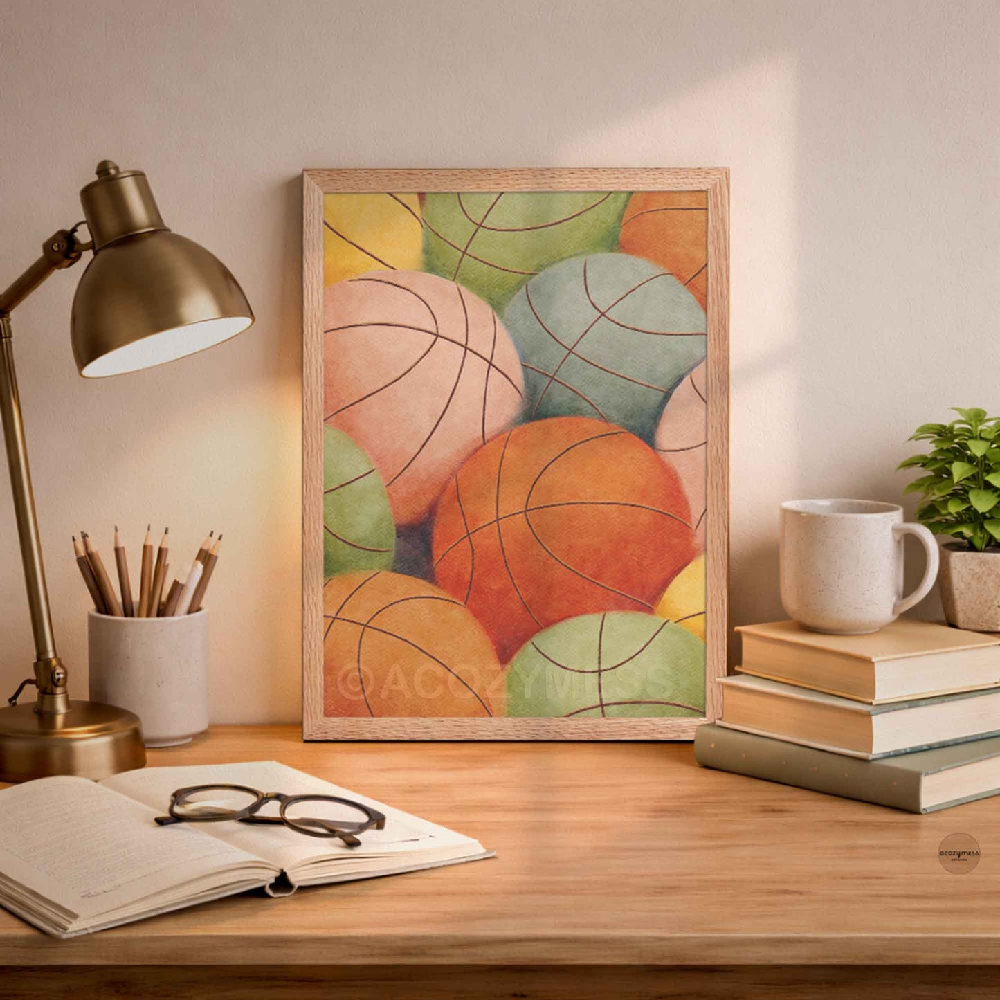 Colorful abstract art print of basketballs in oakwood frame on a desk with a lamp, books, and a mug.