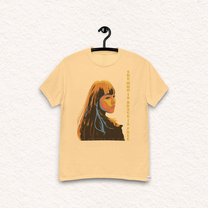 A yellow haze color t-shirt featuring an illustration of a woman and the quote, She who is brave is free, inspired by Seneca. The design reflects strength and elegance, making it perfect for casual and versatile wear.
