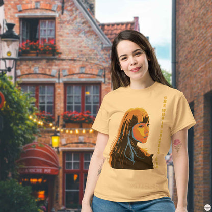 A woman wearing yellow haze t-shirt featuring an illustration of a woman and the quote, She who is brave is free, inspired by Seneca. The design reflects strength and elegance, making it perfect for casual and versatile wear.