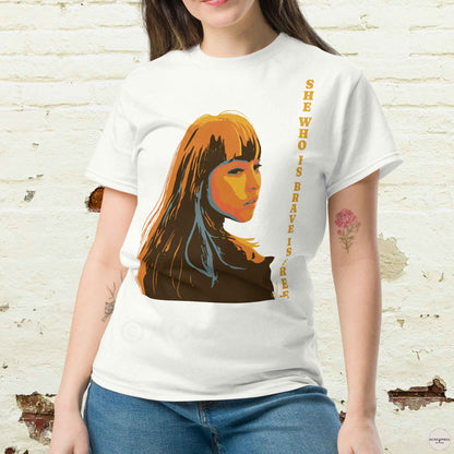 A woman wearing white t-shirt featuring an illustration of a woman and the quote, She who is brave is free, inspired by Seneca. The design reflects strength and elegance, making it perfect for casual and versatile wear.