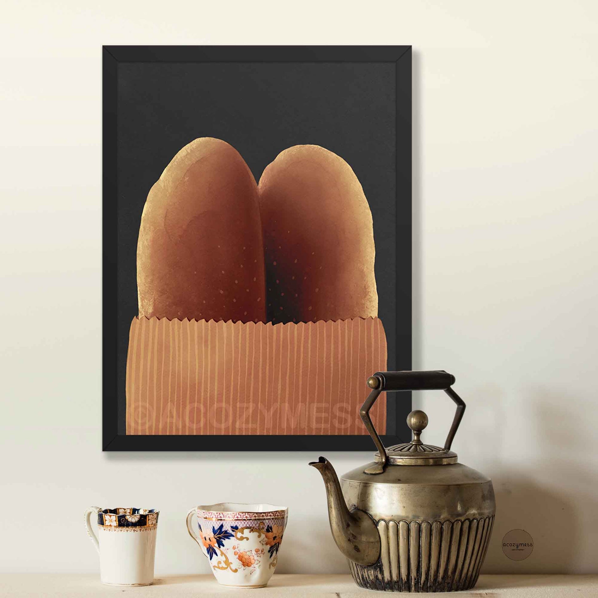 Framed artwork of bread in a loaf bag on a wall above a table with teacups and a teapot.