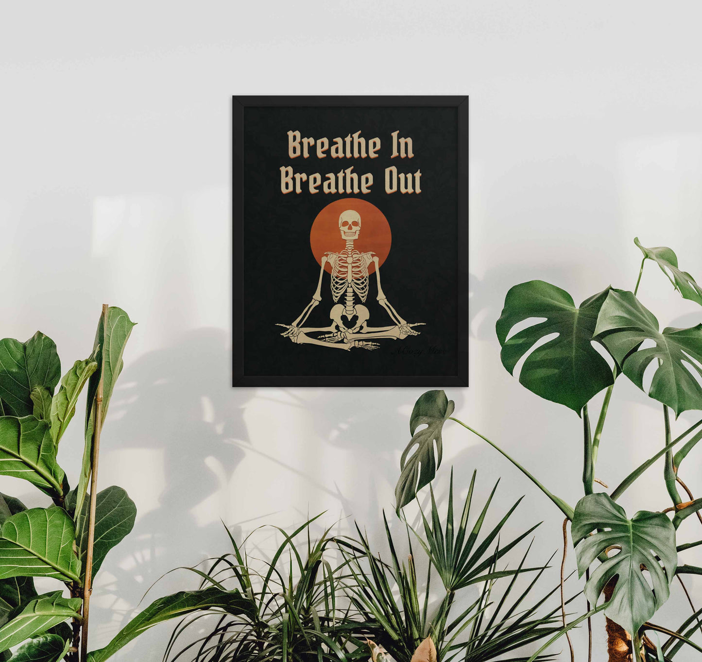 Black framed wall art of " Breathe in breathe Out" with an illustration of a meditating skeleton