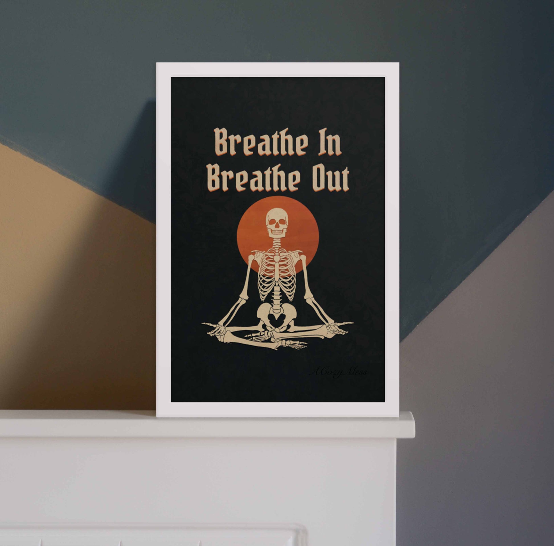 White framed wall art of " Breathe in breathe Out" with an illustration of a meditating skeleton