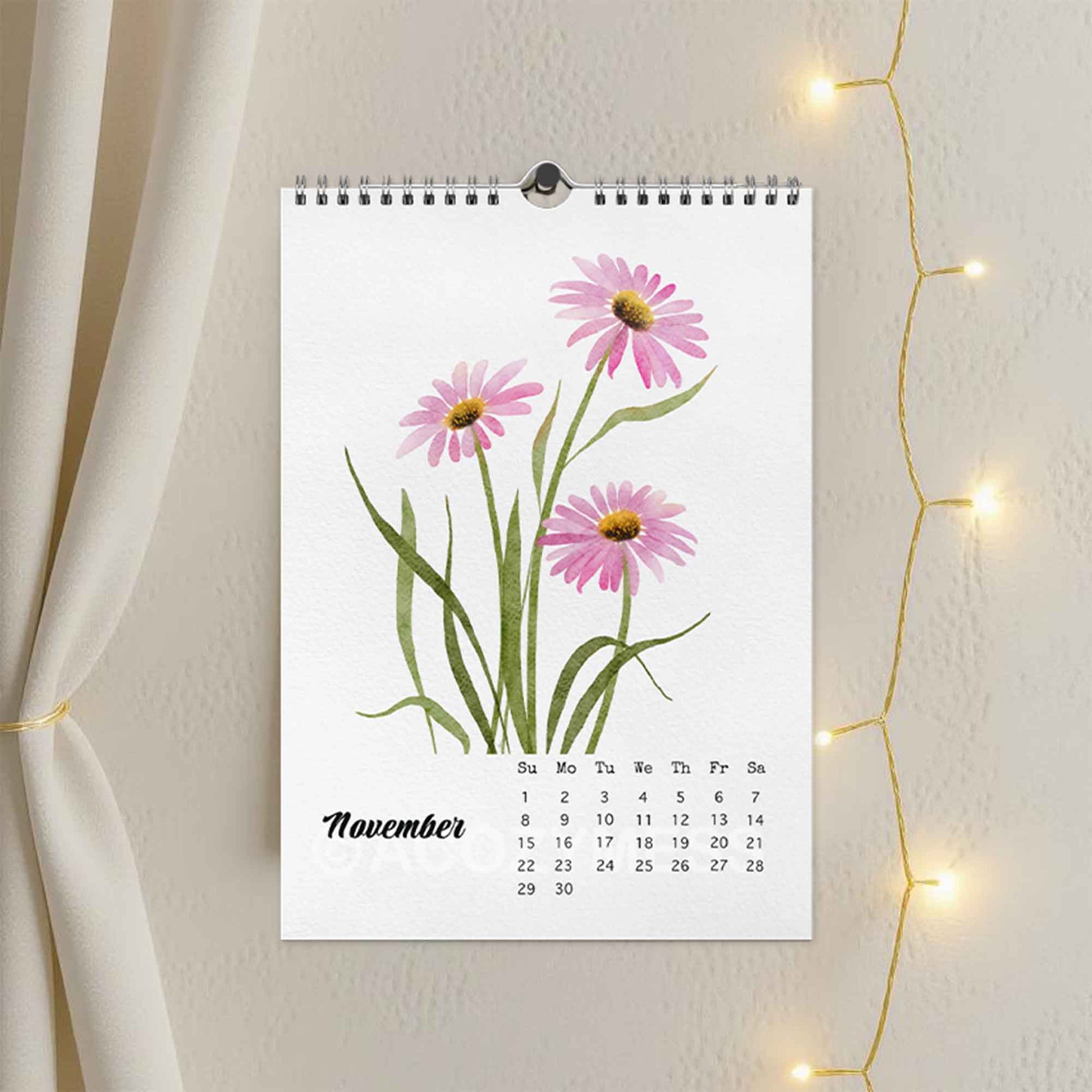 Wall calendar with pink flowers for November on a white wall with string lights.