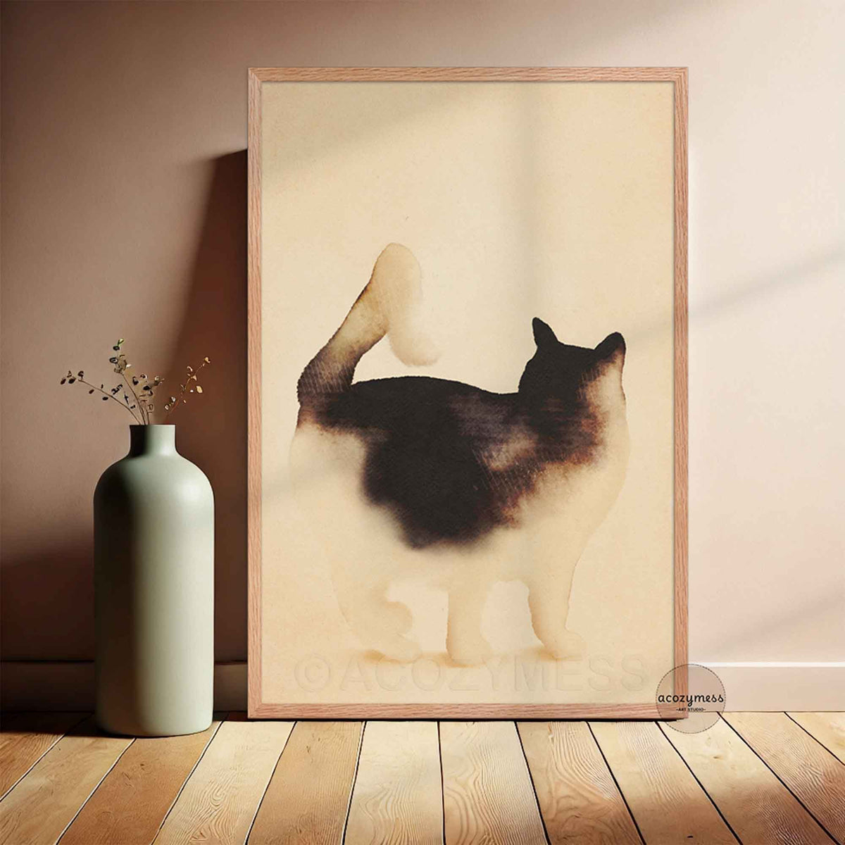 Minimalist watercolor black and white cat art poster in a light oak frame leaning against a warm beige wall beside a sage green vase