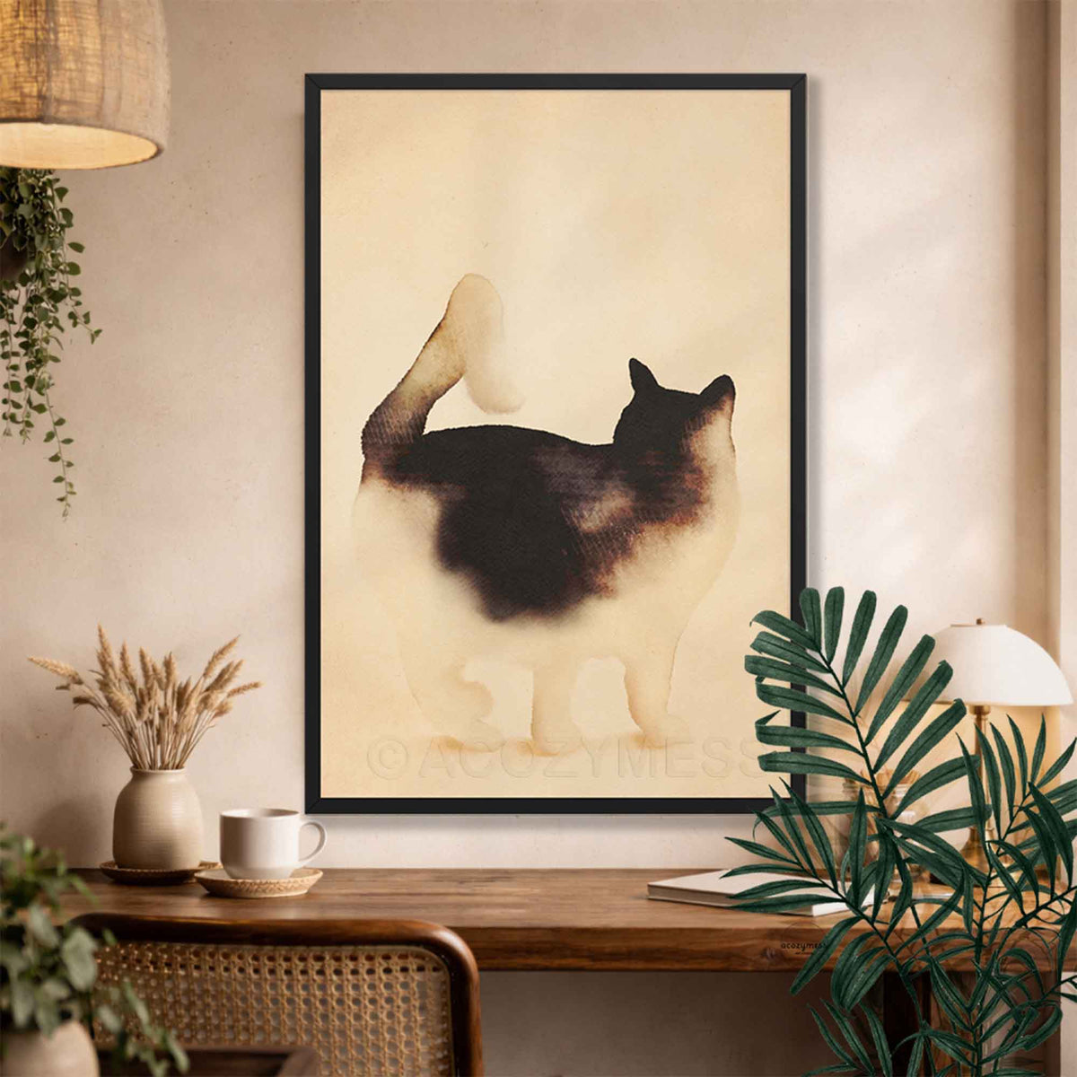 Black framed watercolor cat art print with tail held high above a rustic desk with dried flowers and plants