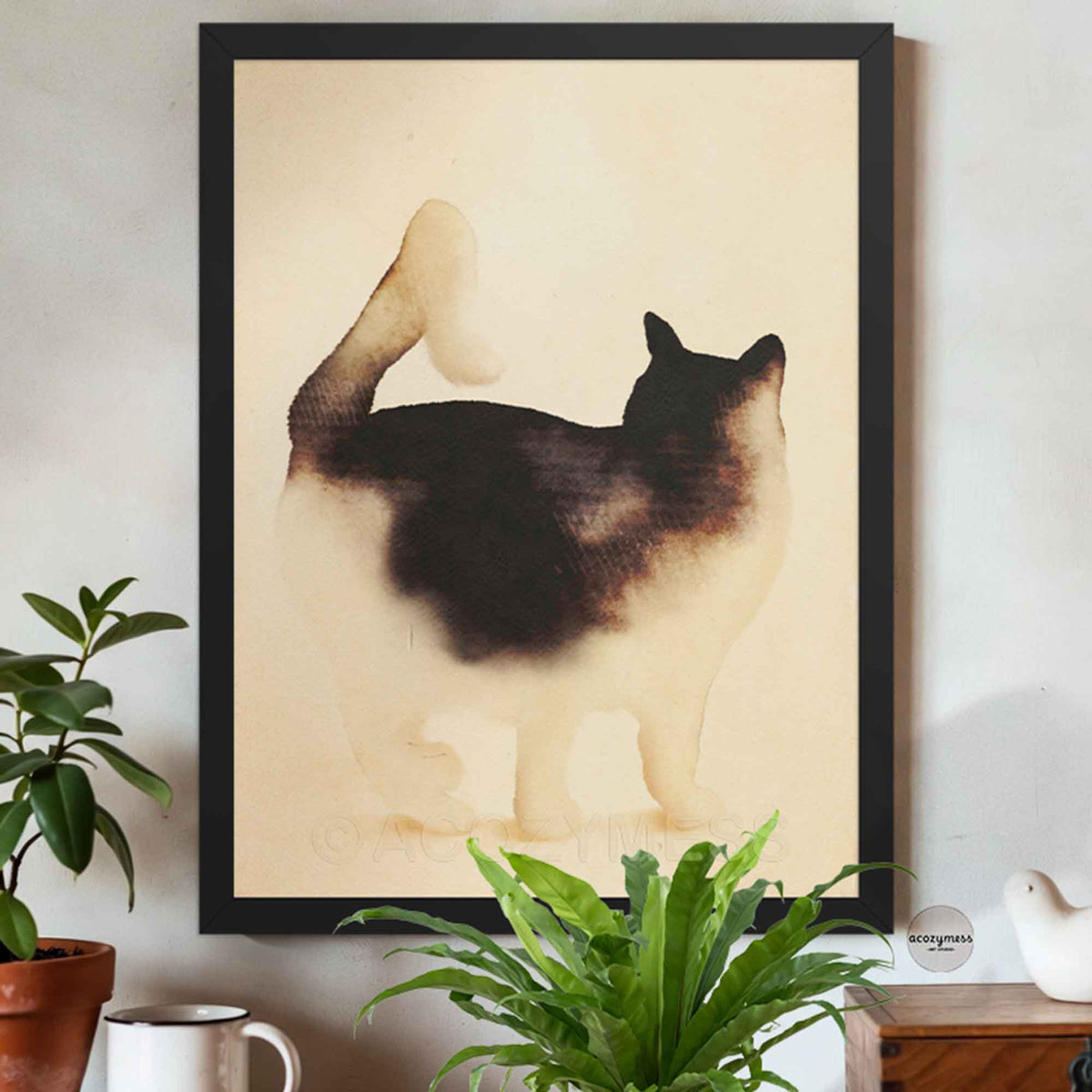 Black framed black and white cat wall art on a cream wall above potted plants