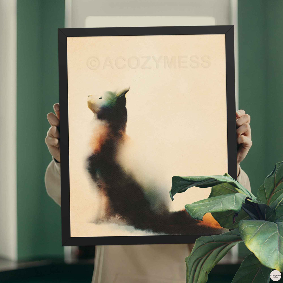 Hands holding a black framed watercolor cat looking up poster in front of a green wall with a fiddle leaf plant