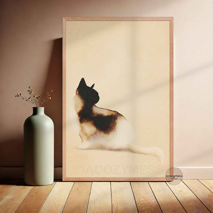 Minimalist watercolor calico cat art poster in a light oak frame leaning against a warm beige wall beside a sage green vase