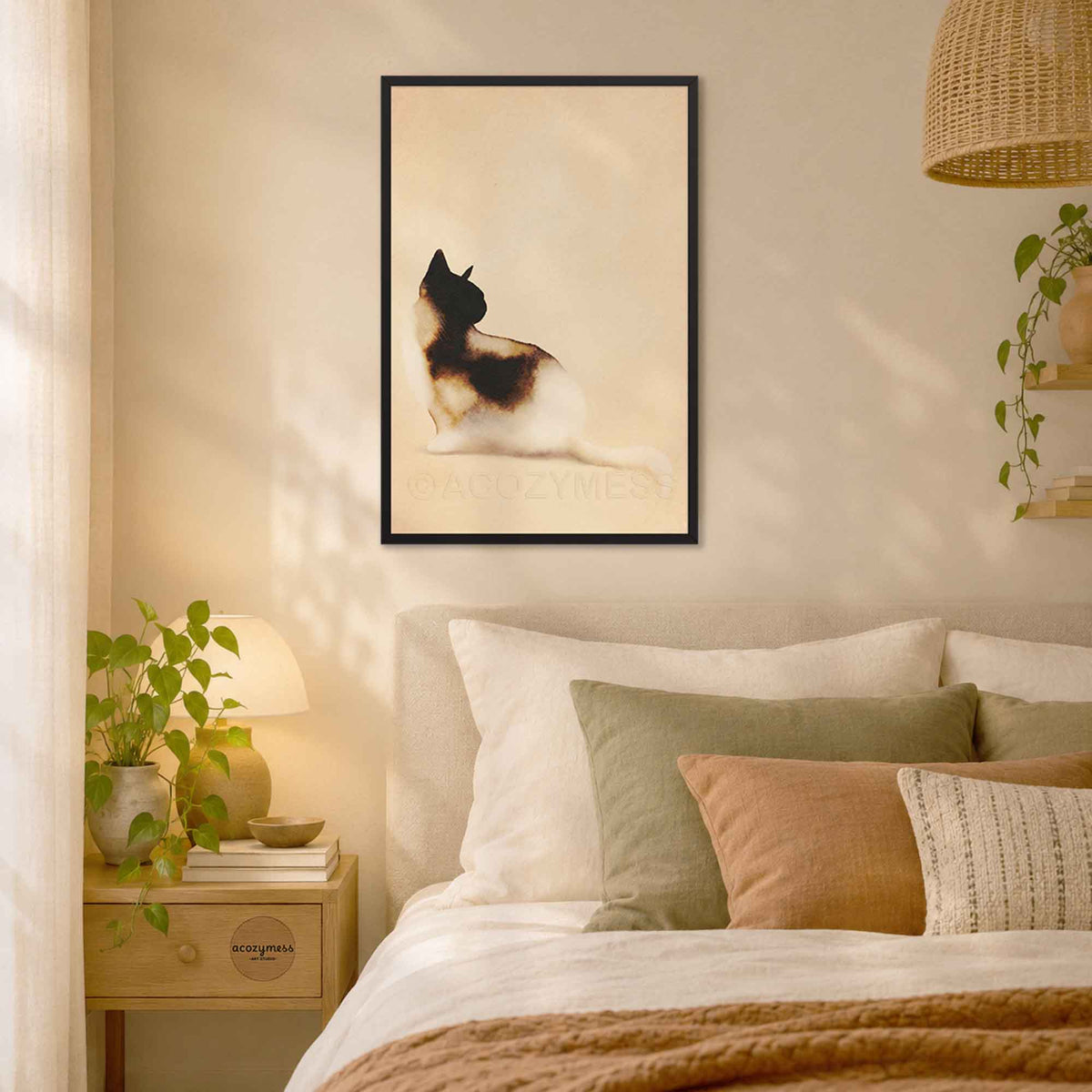 Black framed watercolor cat art print above a bed with soft neutral pillows in a cozy bedroom