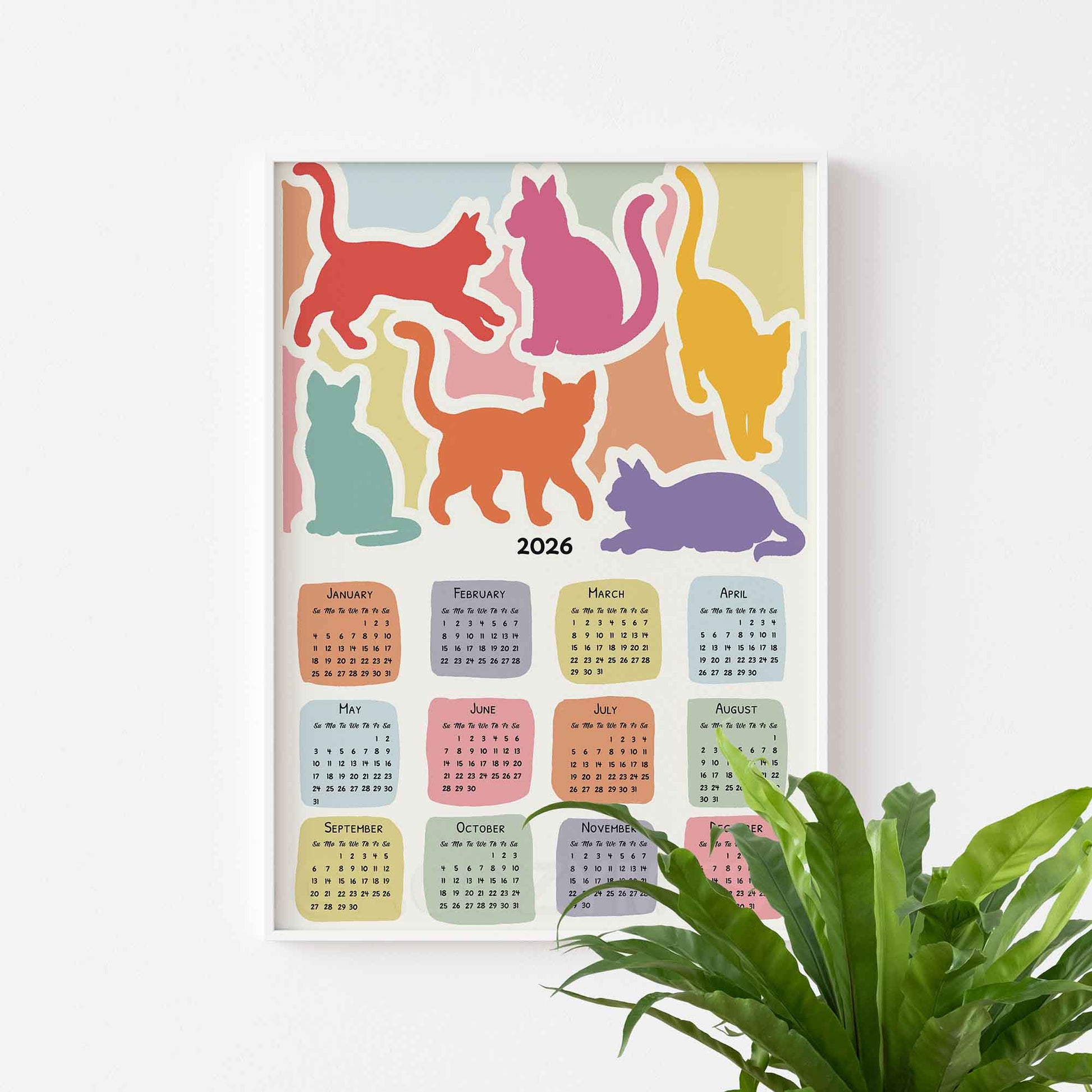 Colorful calendar with cat illustrations for 2026 on a white wall.