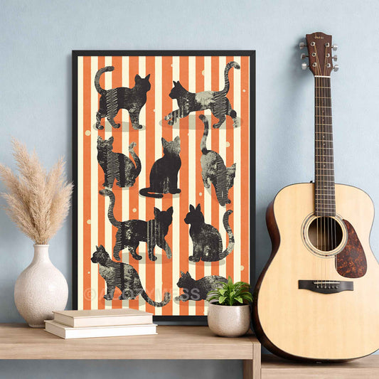 Framed artwork of cats on an orange and white striped background next to a guitar on a wooden surface.