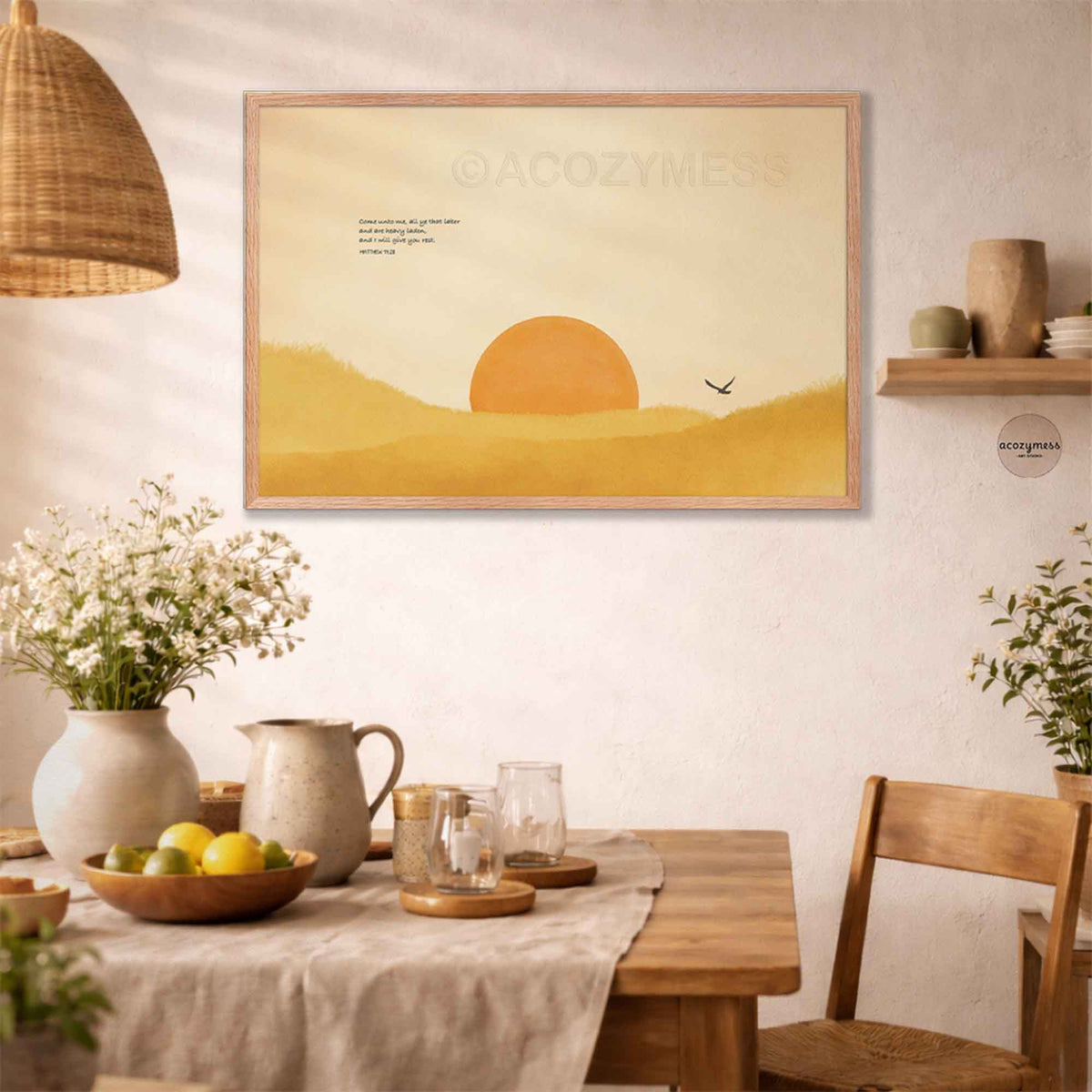 Oak framed Matthew 11:28 sun landscape art print above a rustic dining table with white flowers, a fruit bowl and a rattan pendant lamp