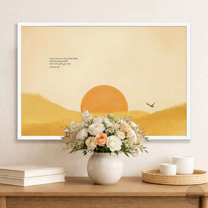 White framed Come Unto Me scripture poster above a wooden console with a white flower bouquet and stacked books